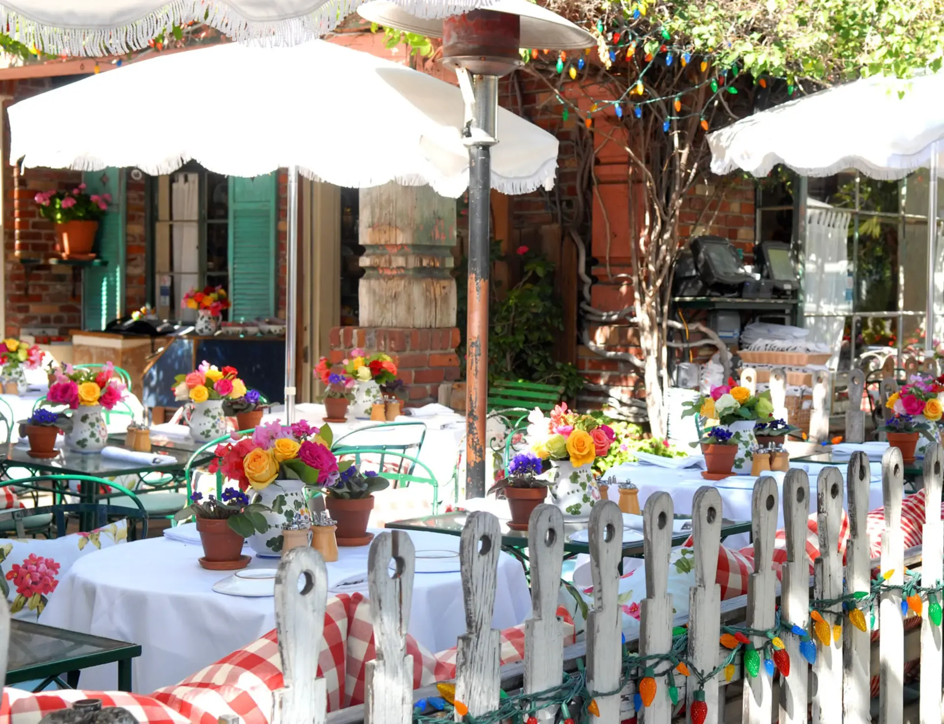The Ivy’s patio behind its white picket fence, with fringed umbrellas, floral tablecloths, and pitchers of fresh roses on every table