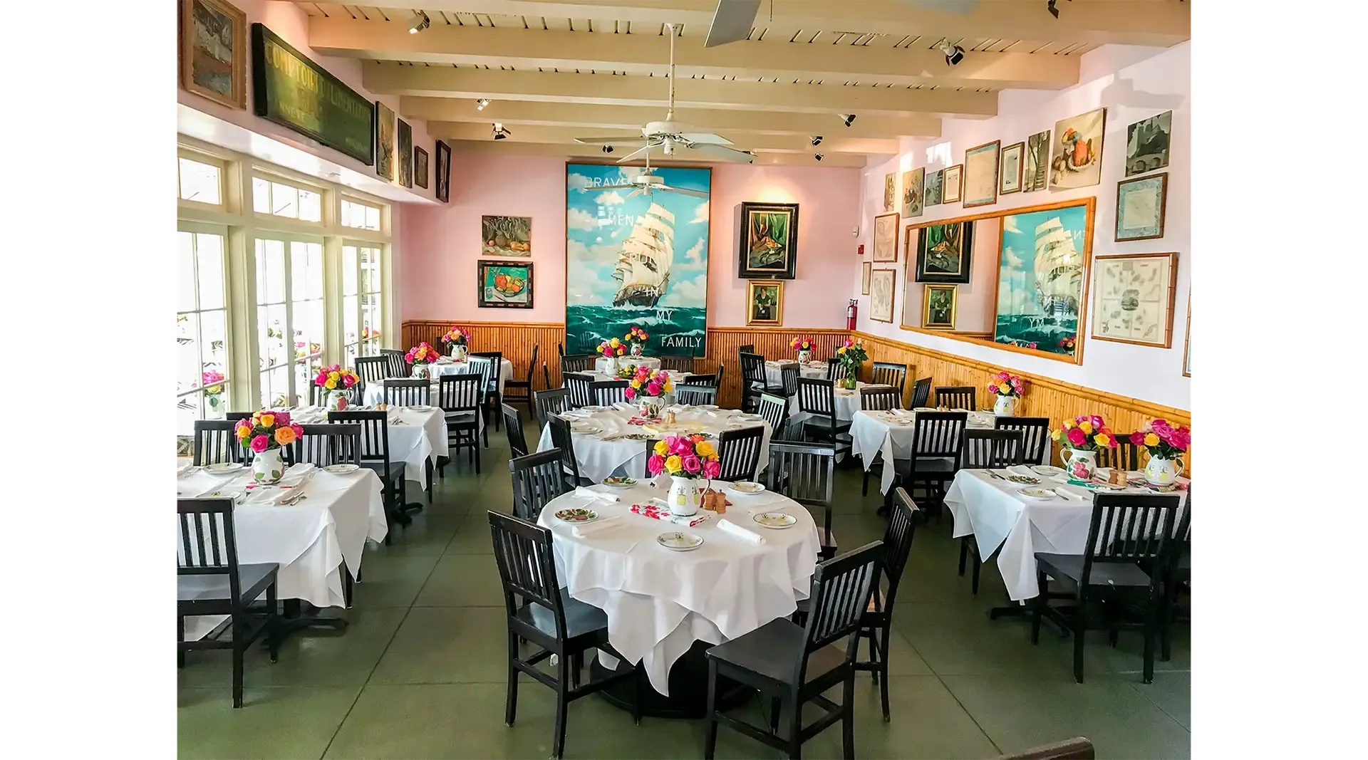 Ivy at the Shore’s dining room with white-clothed tables, pitchers of roses, pink walls, and seaside paintings